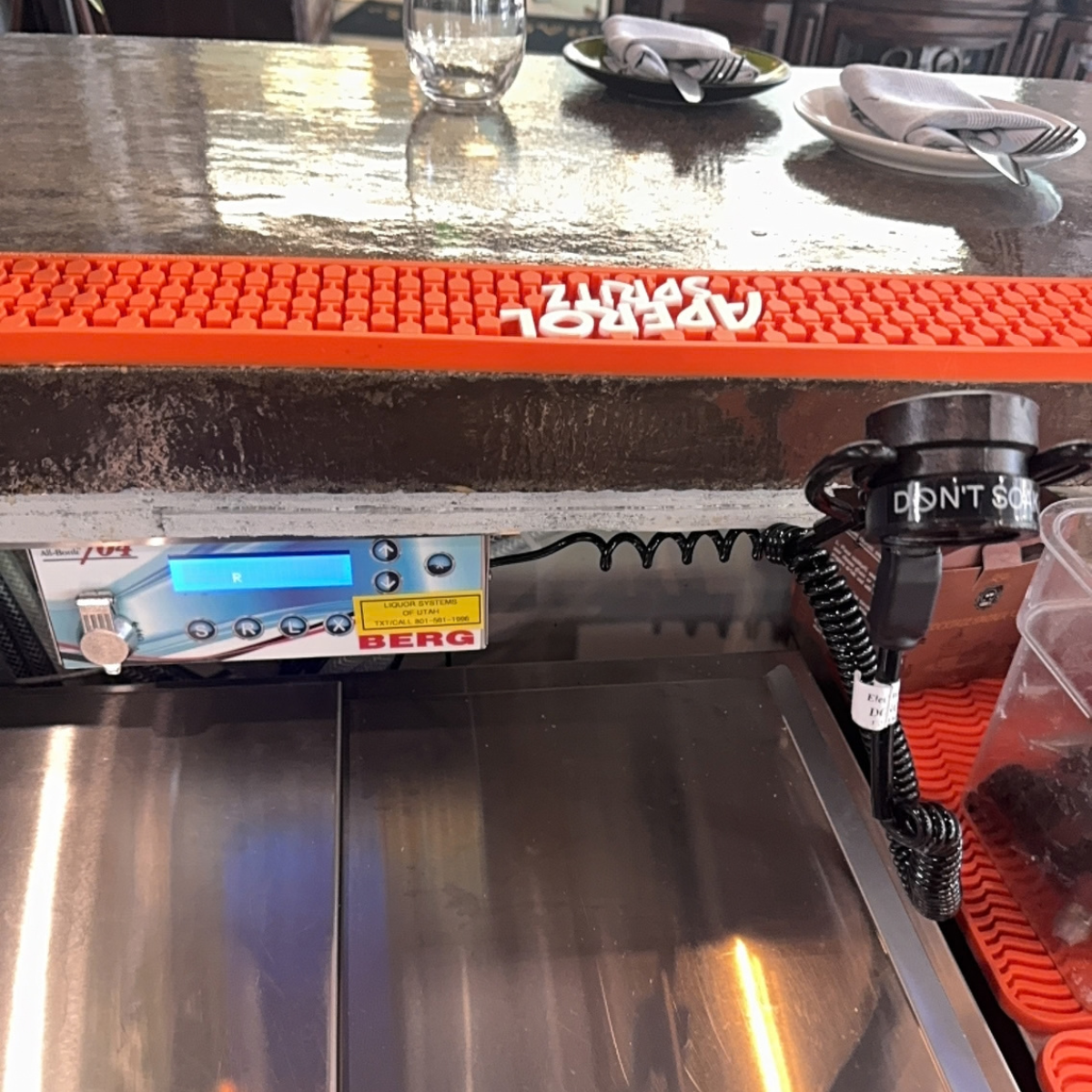 Berg 704 liquor dispensing device, mounted under a bar. Attached ring cord is supported by ring cord holder also mounted under the bar. 